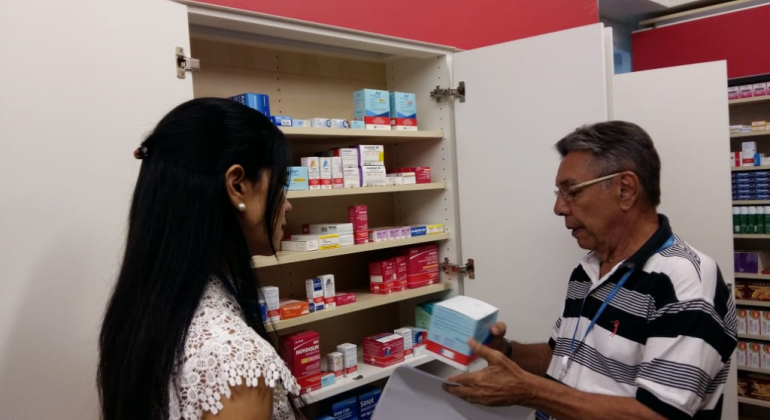 Homem segura antibiótico em frente a armário de medicamentos, ao lado de mulher. 