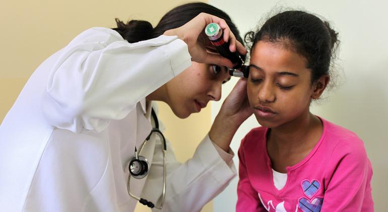 Secretaria de Saúde vai contratar profissionais temporariamente Médica usando jaleco examina criança com lanterna