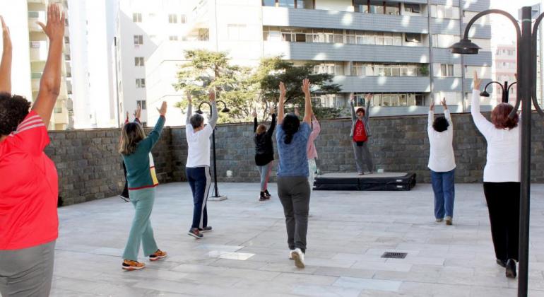 Para estimular a atividade física e promover a saúde da população, a Prefeitura de Belo Horizonte oferece a prática de Lian Gong. Foto: Divulgação PBH Cerca de seis pessoas de mãos para cima, em direção do instrutor, praticando liang gong