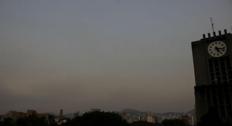 Horizonte nublado e esfumaçado, com detalhe do relógio da PBH à direita, durante o dia. 