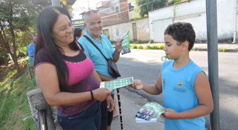 Aluno de escola municipal dá panfleto informativo a moradora de bairro, durante o dia. 