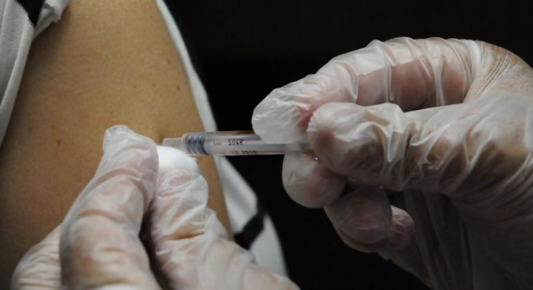 Mão enluvada aplica, com injeção, vacina em braço humano. 