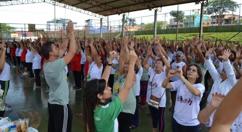 Dezenas de pessoas com as mãos pra cima praticando Lian Gong