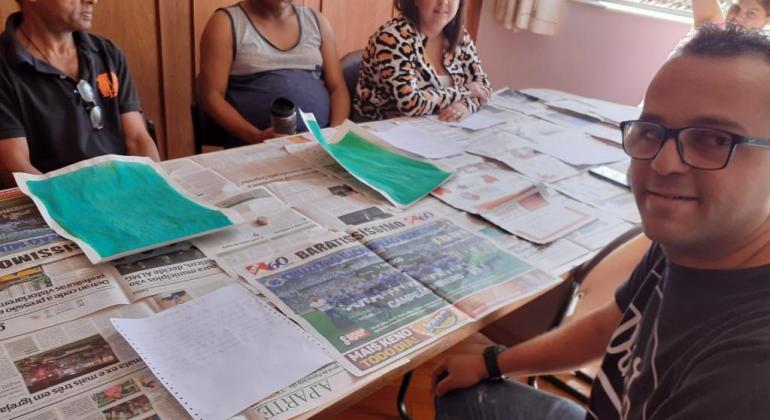 Centros de Convivência da PBH contribuem no processo de reinserção do indivíduo por meio da convivência em atividades prazerosas. Foto: Leila Porto/PBH Cinco pessoas em torno de uma mesa, fazendo oficina de lambe-lambe.