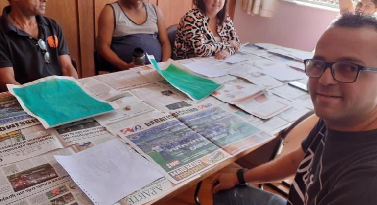 Cinco pessoas em torno de uma mesa, fazendo oficina de lambe-lambe. 