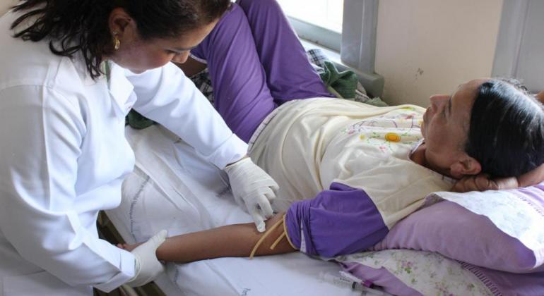 Médica checa braço de paciente, que está deitada. 