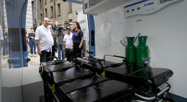 Prefeito Alexandre Kalil, com imprensa ao fundo observa interior de ambulância doada para a saúde de BH. 