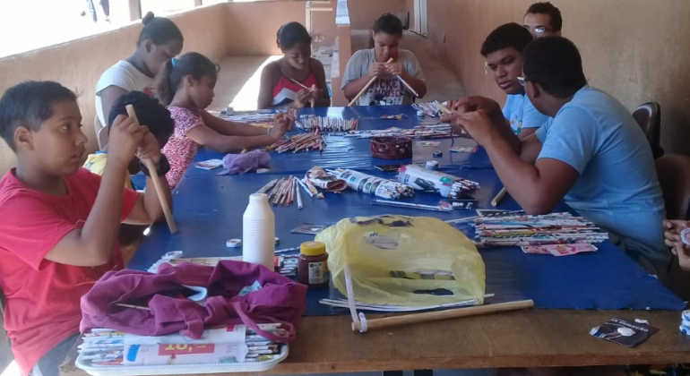 Nove crianças fazem artesanato, durante o dia. 