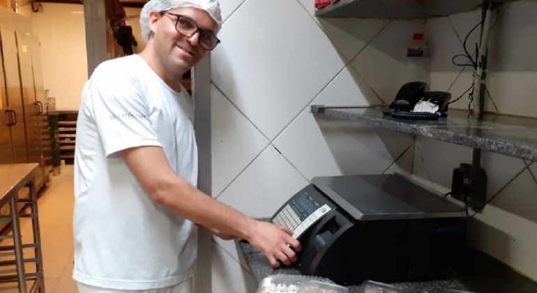 Homem de blusa branca e touca, pesa alimentos.