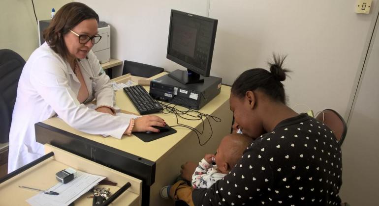 Ambulatório especializado em alergias a proteína do leite de vaca oferece atendimento multiprofissional para crianças. Foto: Leila Porto/PBH Médica atende mãe com seu filho de colo.