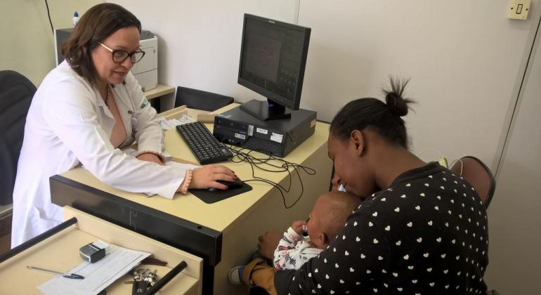 Médica atende mãe com seu filho de colo. 