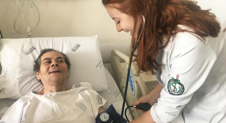 Núcleo de Ensino, Pesquisa e Extensão do Hospital Metropolitano Dr. Célio de Castro receberá 489 estudantes em 2019. Foto: Divulgação PBH Mulher de jaleco branco tira pressão de paciente acamado.