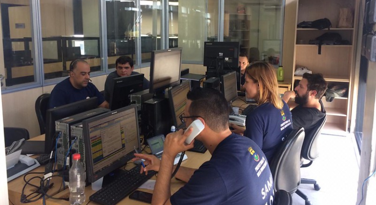 Quatro atendentes do Samu em uma sala com telefones e computadores. 