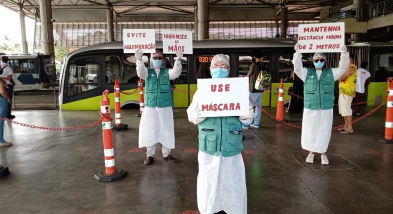 PBH realiza ações de conscientização contra a Covid-19 em estações de ônibus Pessoas com cartazes fazem ato de conscientização sobre Covid-19