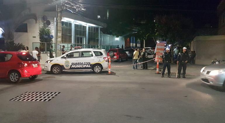 Carro da Guarda Municipal ao lado de dois guardas municipais observando o trânsito. 