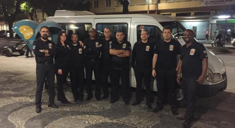 Nove membros da equipe da Guarda Municipal em frente à van, no local em que realizaram operação conjunta de fiscalização, durante a noite. 