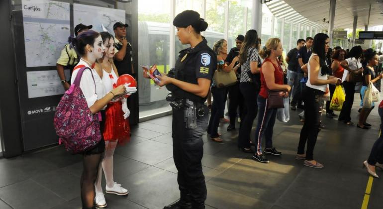 Guarda Municipal distribui panfleto para duas jovens de rosto pintado, foto ilustrativa. 