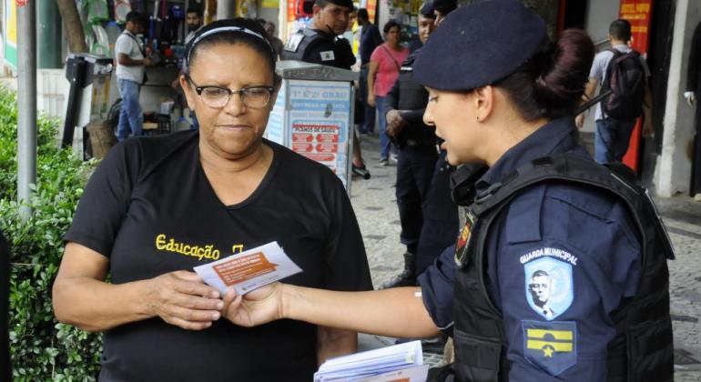 Grupo de Combate à Importunação Sexual no Transporte Público Guarda Municipal entrega folheto a uma mulher na rua