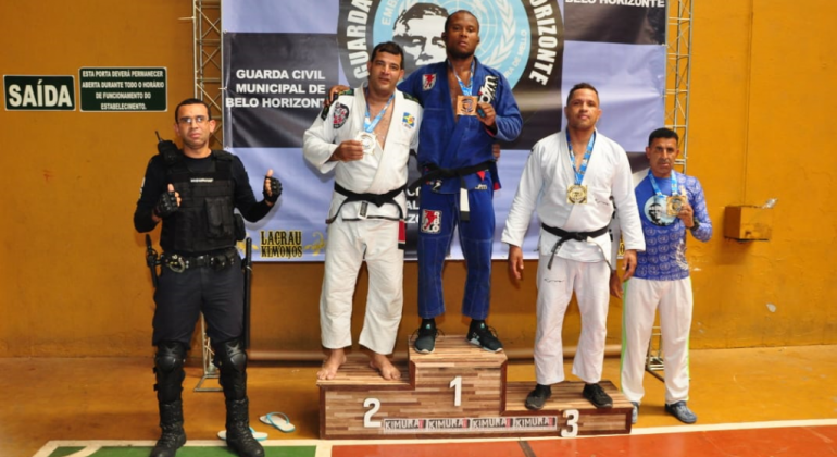 Pódio com três campeões do campeonado de Jiu-jitsu, com dois homens ao lado. 