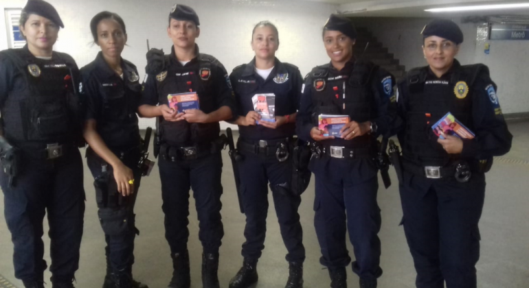 Seis agentes da Guarda Municipal feminina, uniformizadas, com panfleto educativo sobre assédio sexual. 