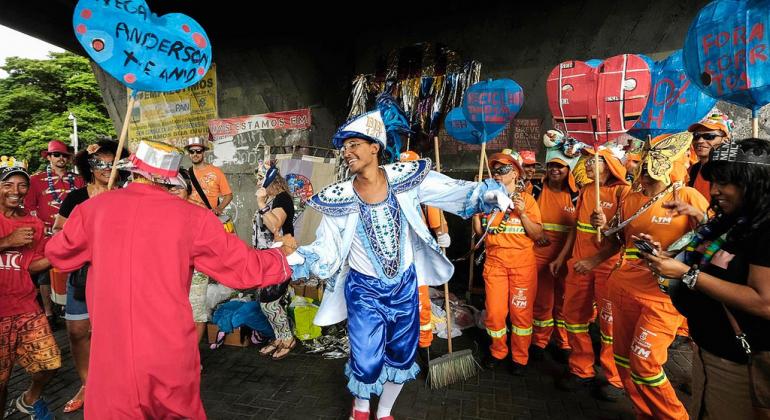 No Carnaval, as vias públicas da capital são limpas antes, durante os intervalos e após a passagem dos blocos carnavalescos. Foto: Marcelo Santos/PBH Foliões dividem espaço com mais de seis funcionários da SLU, uniformizados de gari.