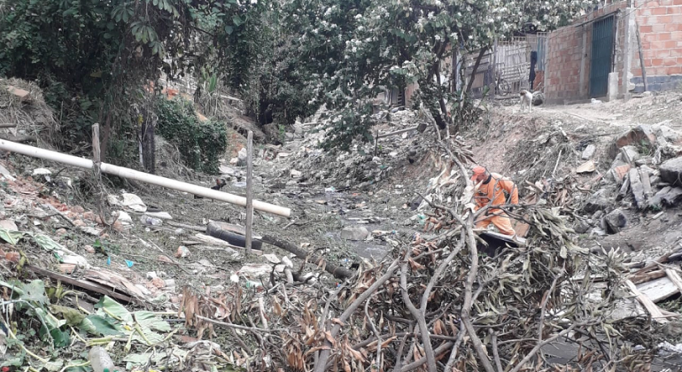 Na terça-feira, dia 13/8, a partir das 8h30, será feita a limpeza do rio Arrudas, na avenida dos Andradas, altura do número 5.695. Foto: Divulgação PBH Funcionário da SLU, vestido de laranja, retira galhos de um córrego, durante o dia.