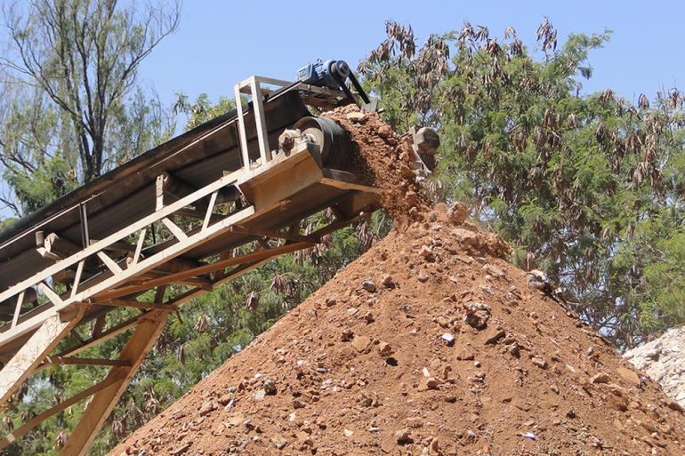 Triturador de resíduos da construção civil em funcionamento formando uma pilha de terra e concreto moídos