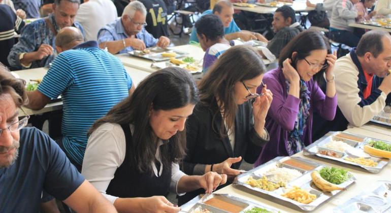 Diversas pessoas sentadas em mesas do Restaurante Popular com bandejas com comidas
