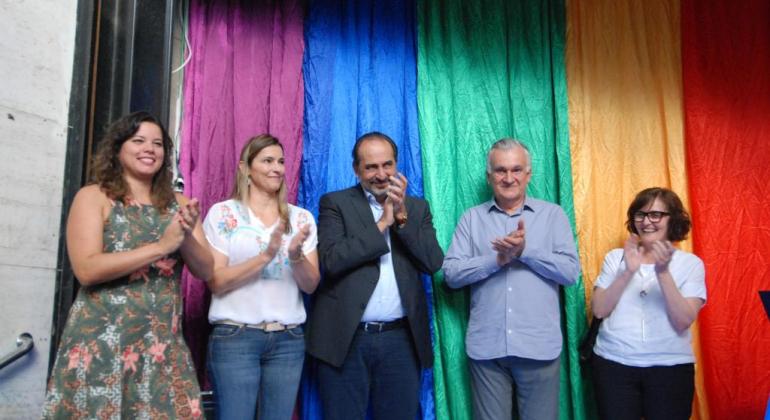 Pessoas em pé em frente a uma bandeira com as cores do arco-íris. Da esquerda para a direita: Maíra Colares, Secretária Municipal de Políticas Sociais, Ana Laender, primeira-dama de Belo Horizonte, Alexandre Kalil, prefeito de Belo Horizonte, Juca Ferreira, secretário municipal de Cultura, Fabíola Moulin, presidente da Fundação Municipal de Cultura