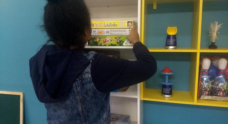 Unidade de Acolhimento Transitório Infantojuvenil dá suporte a jovens em vulnerabilidade social. Foto: Divulgação PBH Criança em situação de vulnerabilidade social escolhe brinquedo em prateleira.