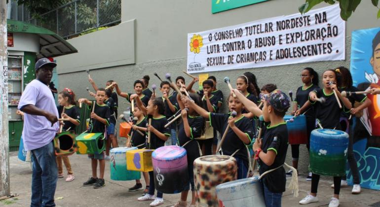 Mais de vinte crianças tocam instrumentos de percussão em evento de protesto contra a exploração sexual de crianças e adolescentes.