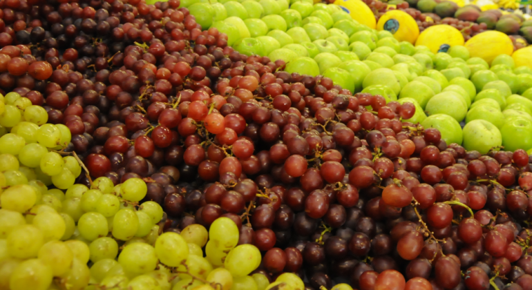 Banca de frutas com uvas verde e roxa, pêra e melão. 