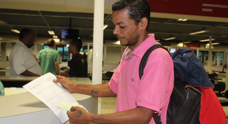 Homem de camiseta pólo rosa e mochila mostra papel, que está em suas mãos. Foto: Patrícia Nogueira/PBH Homem de camiseta pólo rosa e mochila mostra papel, que está em suas mãos.