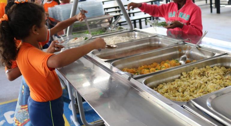 Criança se serve em bandejão em escola municipal. 