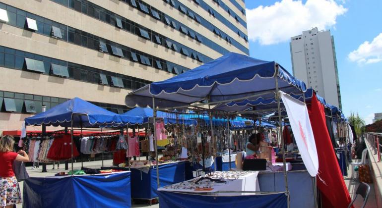 Quatro tendas azuis com artesanato e outras mercadorias, visitadas pelos cidadãos, durante o dia. 