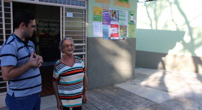 Homem e senhora em frente a centro de referência revitalizado, durante o dia. 