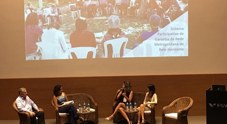 O Sistema Participativo de Garantia da Região Metropolitana é uma das iniciativas de inovação para a inclusão da agricultura familiar. Foto: Viviane Flaviano Quatro pessoas, sentadas, assistem a exposição em painel.