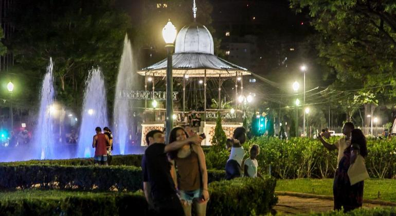 Coreto da Praça da Liberdade à noite, com luzes azuis nos jatos d'água à noite e pessoas tirando foto. 