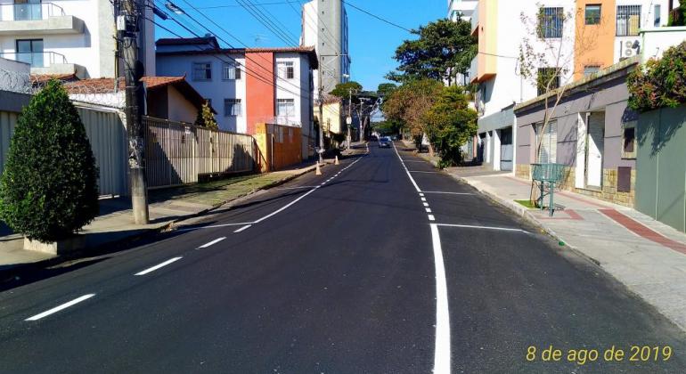 Rua de bairro recapeada, durante o dia. 