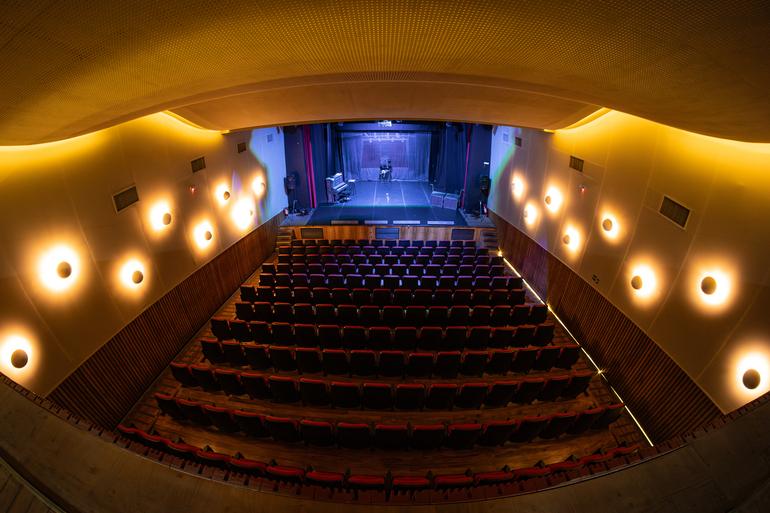 Programação dedicada ao feminino na dança contemporânea ocupa o Teatro Marília Imagem do teatro. Acentos no meio, palco ao fundo iluminado e com as cortinas abertas, luzes redondas nos corredores laterais.