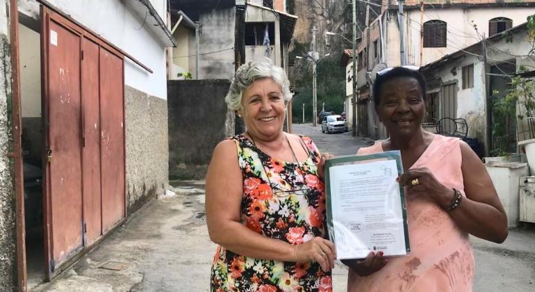 De janeiro de 2017 a maio de 2019, a PBH regularizou 7.052 domicílios e 1.967 unidades habitacionais em BH, beneficiando 9.019 famílias. Foto: Divulgação PBH Duas mulheres mostram título de propriedade.