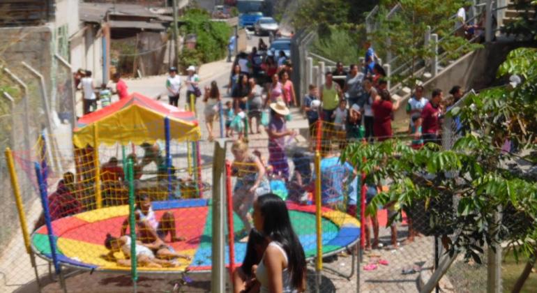 Espaço aberto com pula-pula e outros brinquedos infantis, com mais de vinte pessoas, durante o dia. 