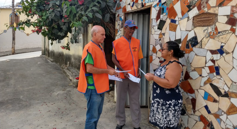 A PBH, através da Urbel, atua permanentemente para diagnosticar, prevenir e minimizar as situações de risco no período chuvoso. Foto: Divulgação PBH Dois técnicos da Urbel mostram material informativo à moradora.