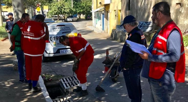 Em junho, PBH realizou diversas vistorias conjuntas com os voluntários dos Núcleos de Alerta de Chuva e diversos órgãos municipais. Foto: Divulgação PBH Cinco funcionários e técnicos conferem se bueiro está desentupido em rua de Belo Horizonte, durante o dia.