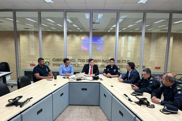 Gestores reunidos ao redor de uma grande mesa em formato de U em uma sala de reuniões, tendo ao fundo divisórias de vidro com a inscrição "Centro de Operações da Prefeitura de Belo Horizonte"