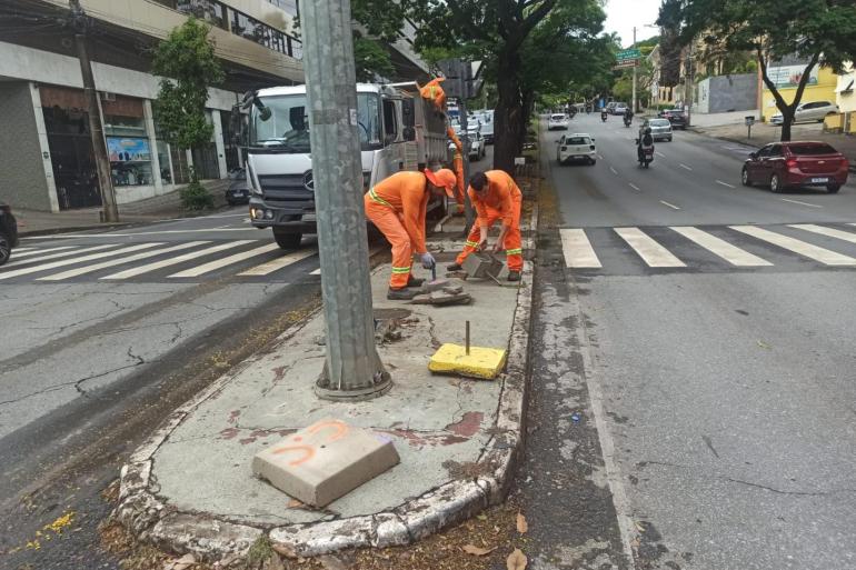 SLU divulga balanço parcial dos resíduos gerados nas Eleições 2026 A foto mostra uma equipe de trabalhadores da limpeza urbana realizando serviços de manutenção em um canteiro central de uma avenida. Os profissionais, uniformizados com roupas laranjas e faixas refletivas, trabalham próximos a um caminhão de coleta, utilizando ferramentas manuais para retirar resíduos e realizar reparos no piso. Em primeiro plano, há uma base de concreto e um poste instalado no canteiro, além de materiais e resíduos resultantes do serviço. Ao fundo, é possível ver o fluxo de veículos.