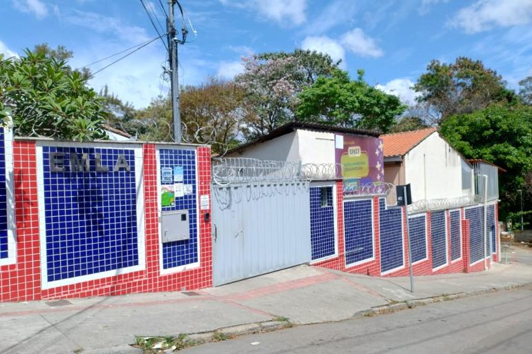 Alunos da Escola Municipal Lídia Angélica iniciam aulas em novos endereços a partir de 19 de outubro Vista externa da Escola Municipal de Educação Infantil (EMEI), com fachada revestida em azulejos nas cores azul, vermelho e branco, portão de entrada e muro de proteção. Ao fundo, aparecem árvores e o céu azul com nuvens.