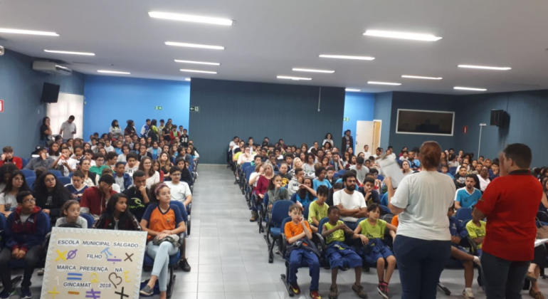 Atividades da Gincamat Jovens estão em um auditório olhando para dois palestrantes