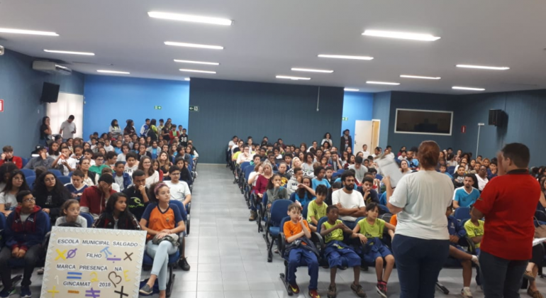 Jovens estão em um auditório olhando para dois palestrantes