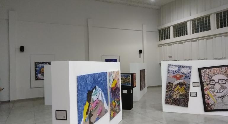 a imagem mostra uma sala onde se vê quadros expostos em 1º e 2º planos, cerca de oito obras de arte .